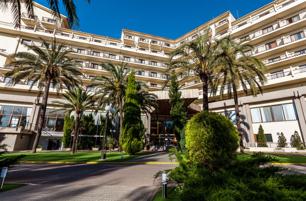Fachada y entrada del hotel con palmeres y vegetación